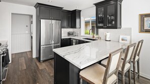 Une cuisine moderne avec des meubles de couleur sombre, un réfrigérateur en acier inoxydable et un îlot en marbre agrémenté de tabourets de bar.