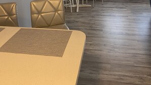 A dining area with a round table and chairs, a clock on the wall, a small round table with a vase, and a window with curtains. - Located right outside of the Vibe District at the Virginia Beach Oceanfront (Virginia Beach)