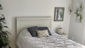 A bedroom with a bed, a ceiling fan, a bedside table with a lamp, and a wall-mounted mirror. - Located right outside of the Vibe District at the Virginia Beach Oceanfront (Virginia Beach)