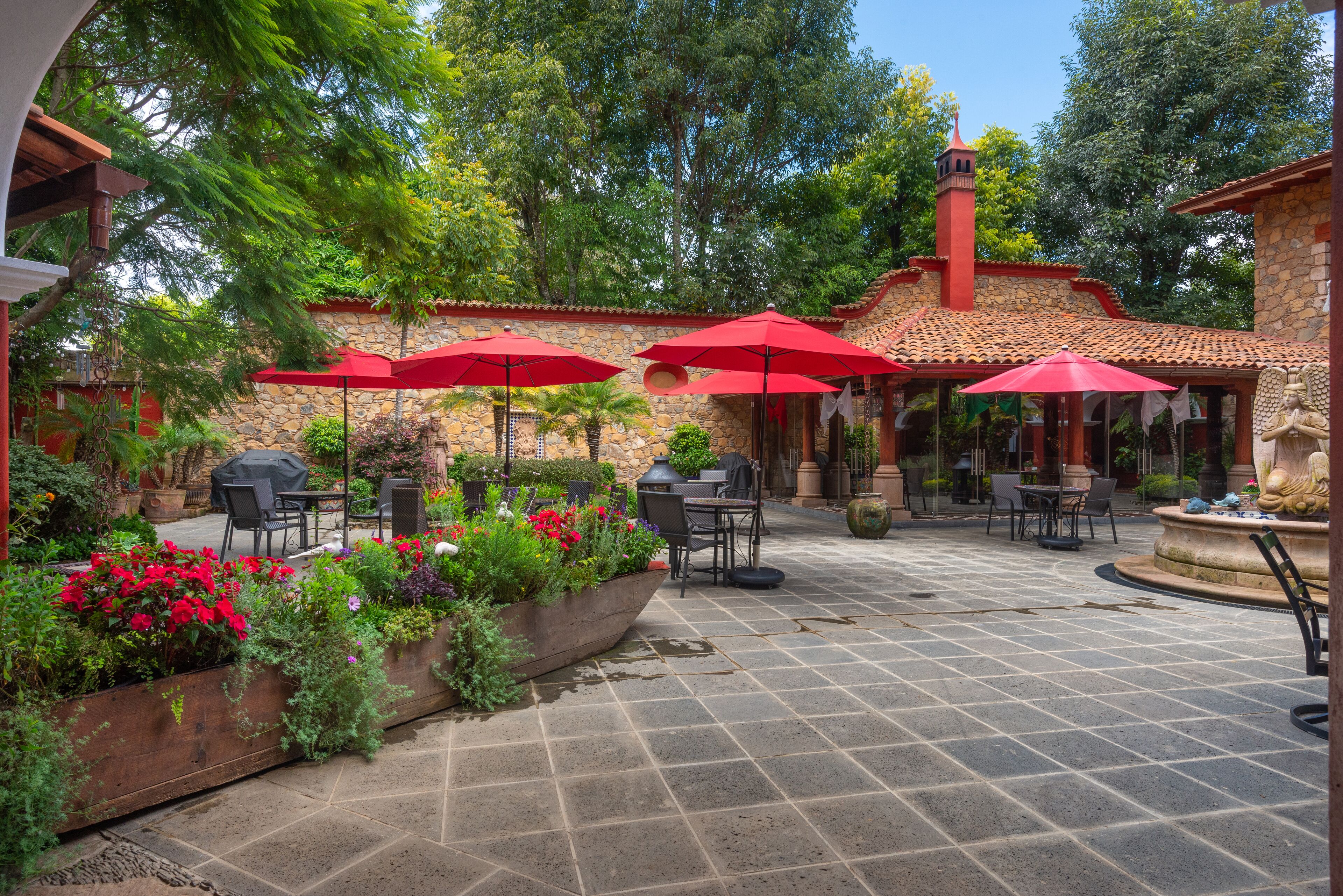 Un patio exterior con suelo de piedra, sombrillas rojas y mobiliario para exteriores.