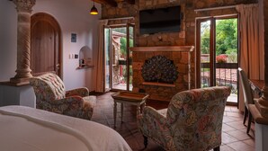 A room with a stone fireplace, two upholstered chairs, a small table, and a TV mounted on the wall. - Hotel Boutique & Spa Casa Colorada (Patzcuaro)