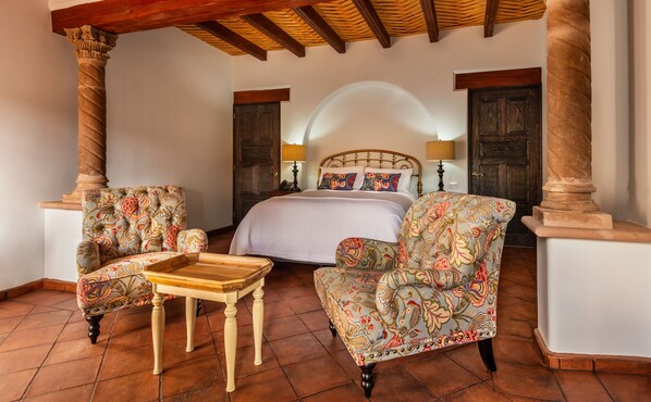 Un dormitorio con una cama, dos sillones, una mesita y techo de madera.