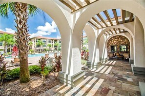 A covered outdoor area with a pool, palm trees, and a stone-tiled floor.