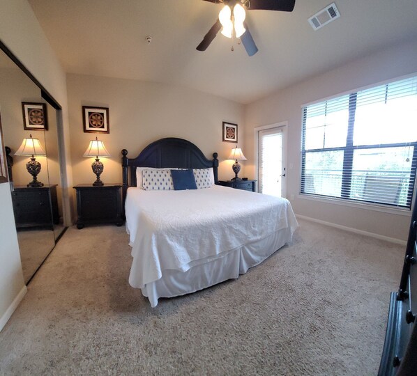 A bedroom with a bed, two bedside tables with lamps, a ceiling fan, and a window with blinds.