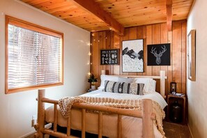 Ein schlafgemach mit Holzwandverkleidung, einem Bett, einem Fenster mit Jalousien und Wandbildern, darunter ein Hirschkopf und ein Wildtierposter.