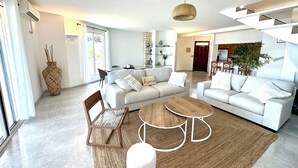 Ein modernes Wohnzimmer mit einer Couch, einem Couchtisch, einem Sessel, einer Treppe und einem Essbereich.