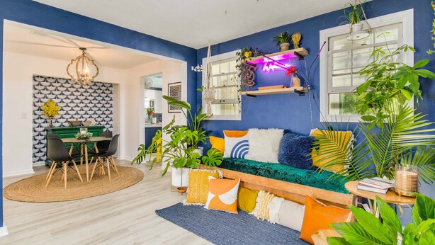A modern living room with a blue accent wall, a dining area with a patterned wallpaper, and various plants and decorative pillows. - NAS, Pensacola Beach, Pool House -20mins to both beaches (Pensacola)