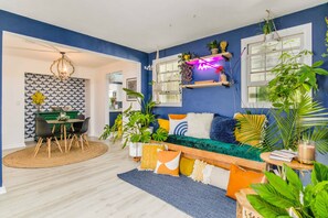 A modern living room with a blue accent wall, a dining area with a patterned wallpaper, and various plants and decorative pillows. - NAS, Pensacola Beach, Pool House -20mins to both beaches (Pensacola)