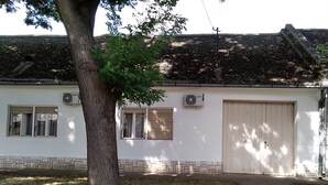 Un bâtiment avec un toit recouvert de tuiles, un grand arbre devant et une porte de garage.
