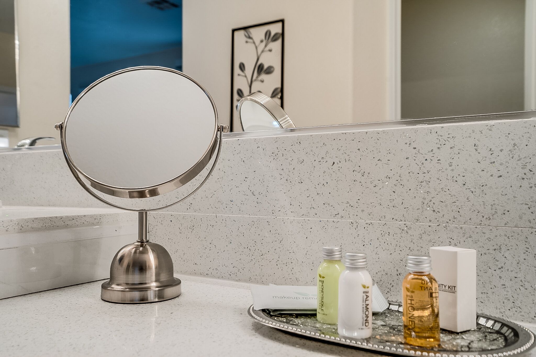 A bathroom vanity with a round mirror, a tray with toiletries, and a framed artwork on the wall.