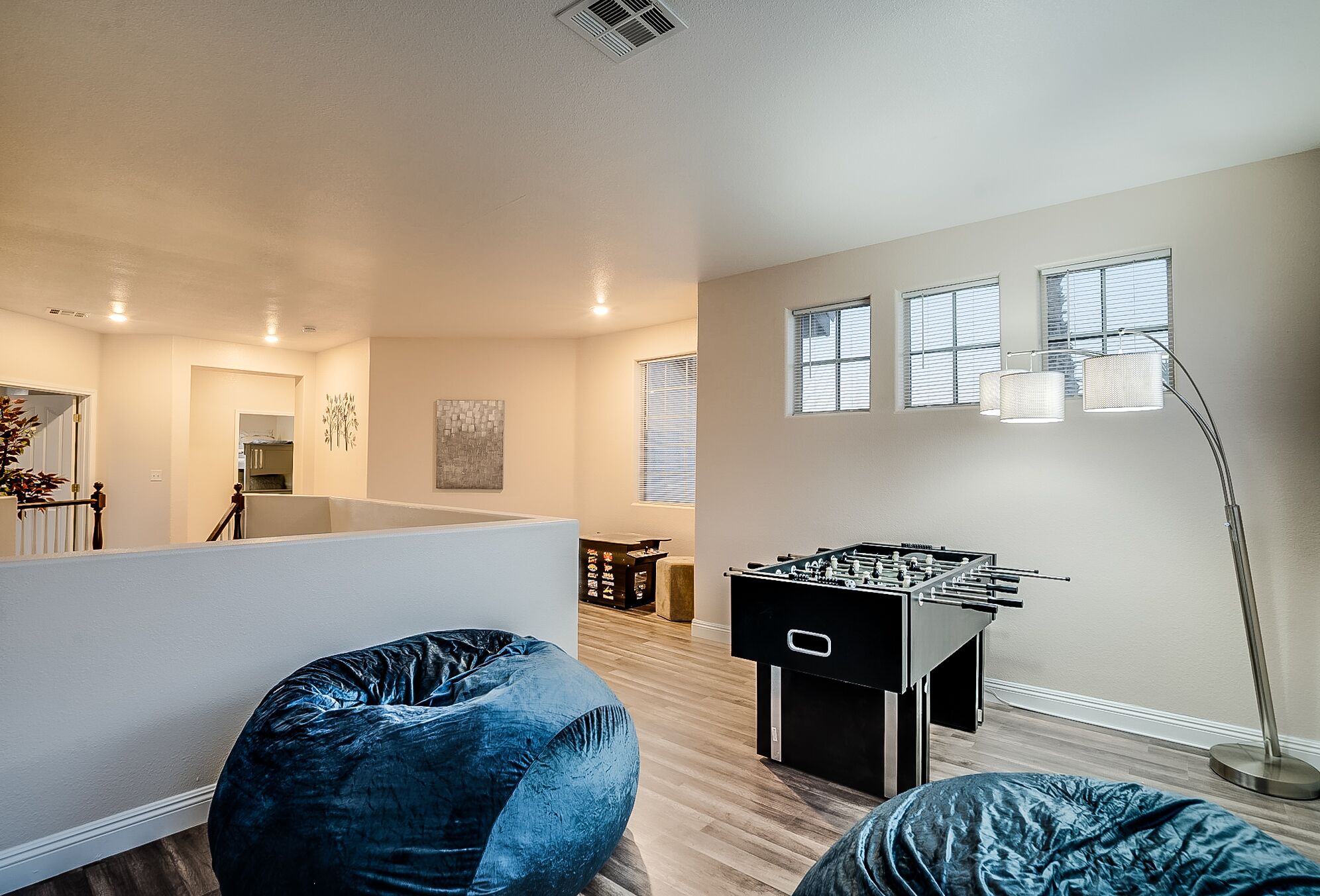 A spacious living room with a foosball table, a bean bag chair, and a modern floor lamp.