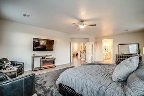 Une chambre à coucher moderne avec un grand lit, une cheminée, un téléviseur et un ventilateur de plafond.