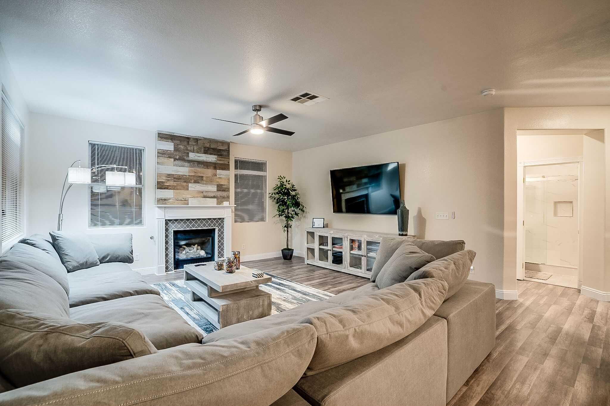 Un salon moderne avec un canapé d’angle, une cheminée, un téléviseur à écran plat et un ventilateur de plafond.
