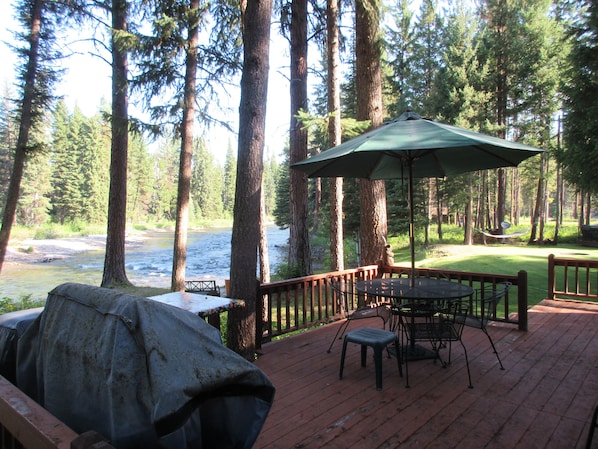 Enjoy a riverside retreat with a deck, table, and grill, surrounded by tall trees.