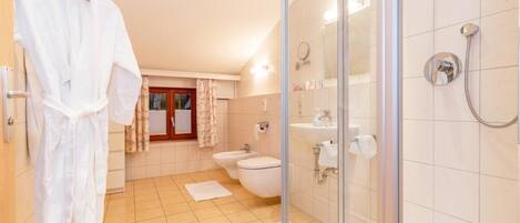 A modern bathroom with a glass-enclosed shower, a bathtub, a toilet, and a bidet.