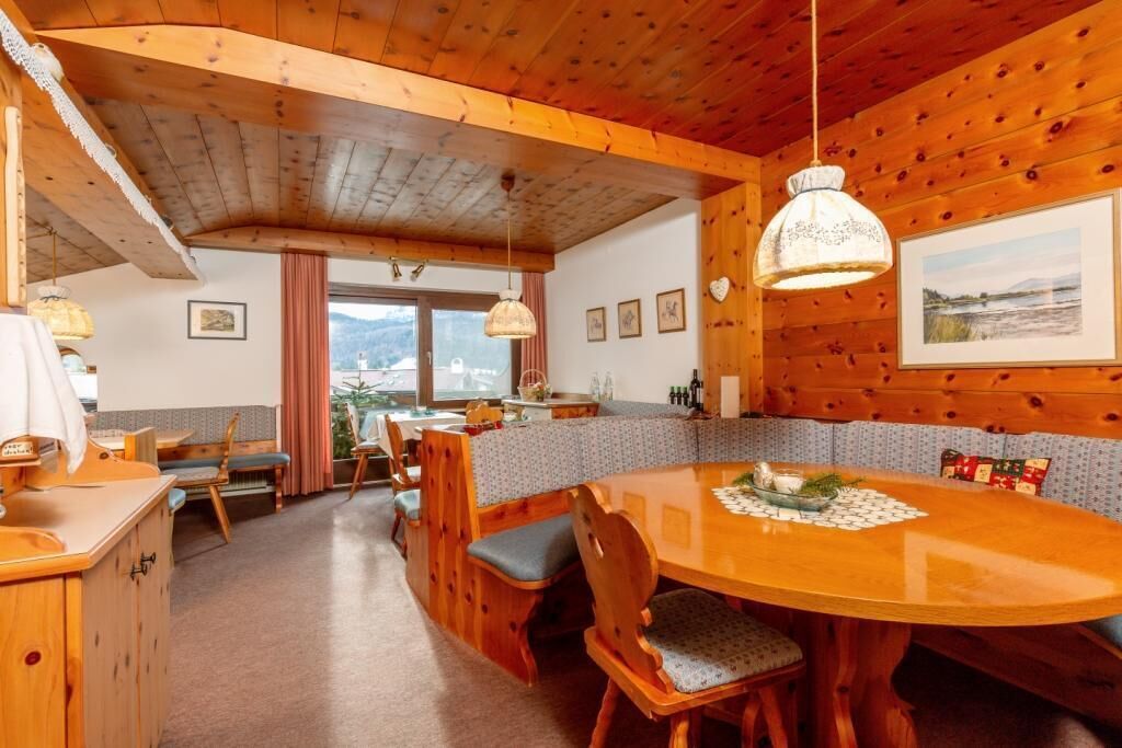 A wooden cabin interior with a dining table, chairs, and a kitchen area.