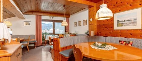 Interior de una cabaña de madera con una mesa de comedor, sillas y una zona de cocina.