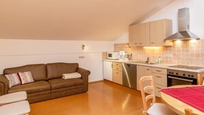 Een kleine keuken met een fornuis, magnetron en vaatwasser. Het plafond is van hout en er is een eethoek met een tafel en stoelen.