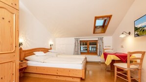 Een slaapkamer met een houten bed, een raam met gordijnen, een tafel met een rode tafelkleed en een stoel.