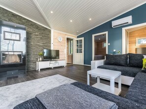 A modern living room with a flat-screen TV, a white coffee table, a grey sofa, and a stone-textured wall.