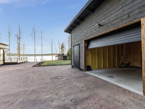 A building with a garage door open, a gravel driveway, and a view of a lake with trees. - Metsola by Interhome (Ruovesi)