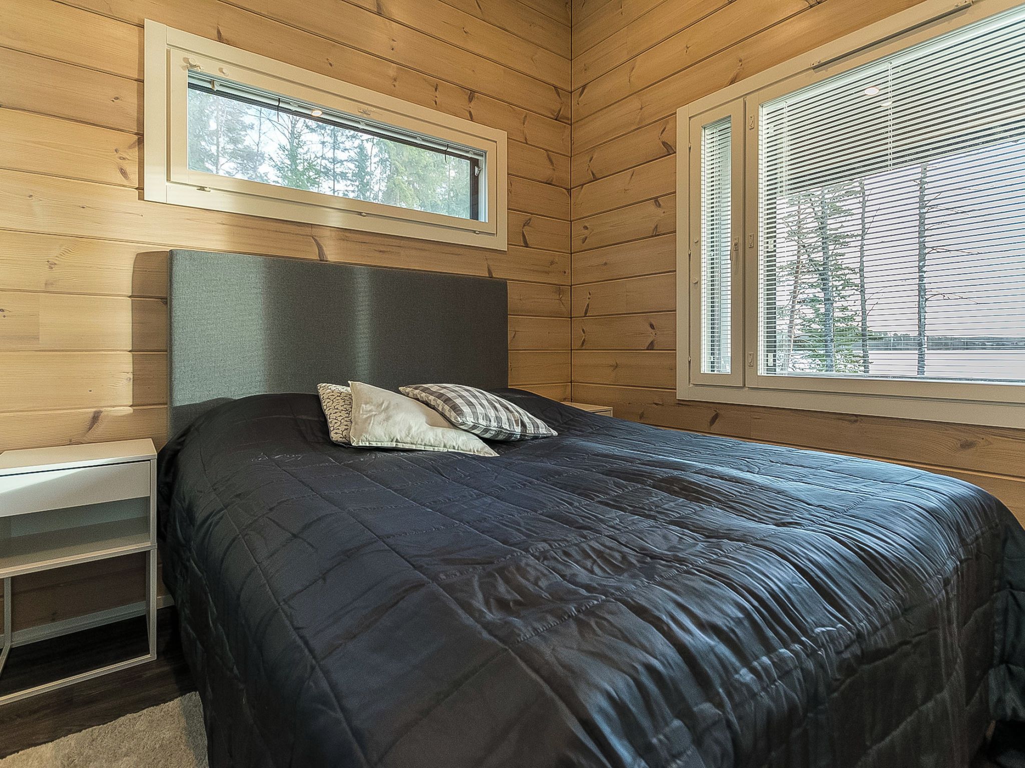 A bedroom with a bed, a nightstand, a window, and a view of trees.
