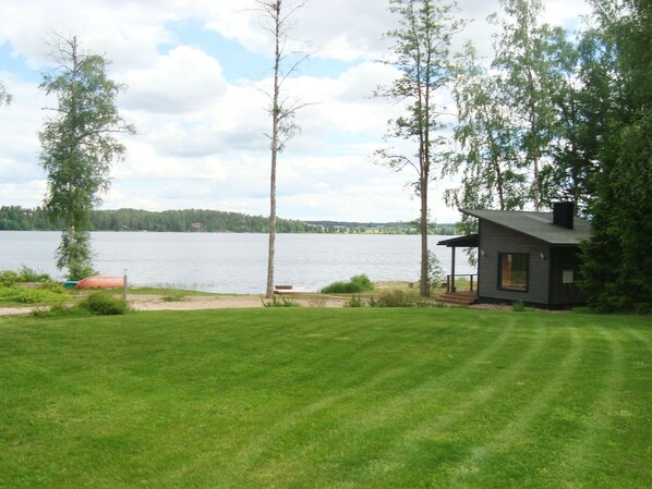 A lakeside property with a grassy lawn, a small cabin, and a boat docked by the water.