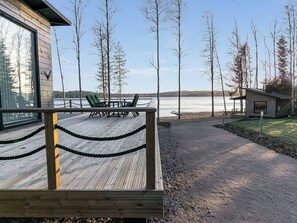 A wooden deck with a rope barrier, a table with chairs, and a view of a lake and trees.