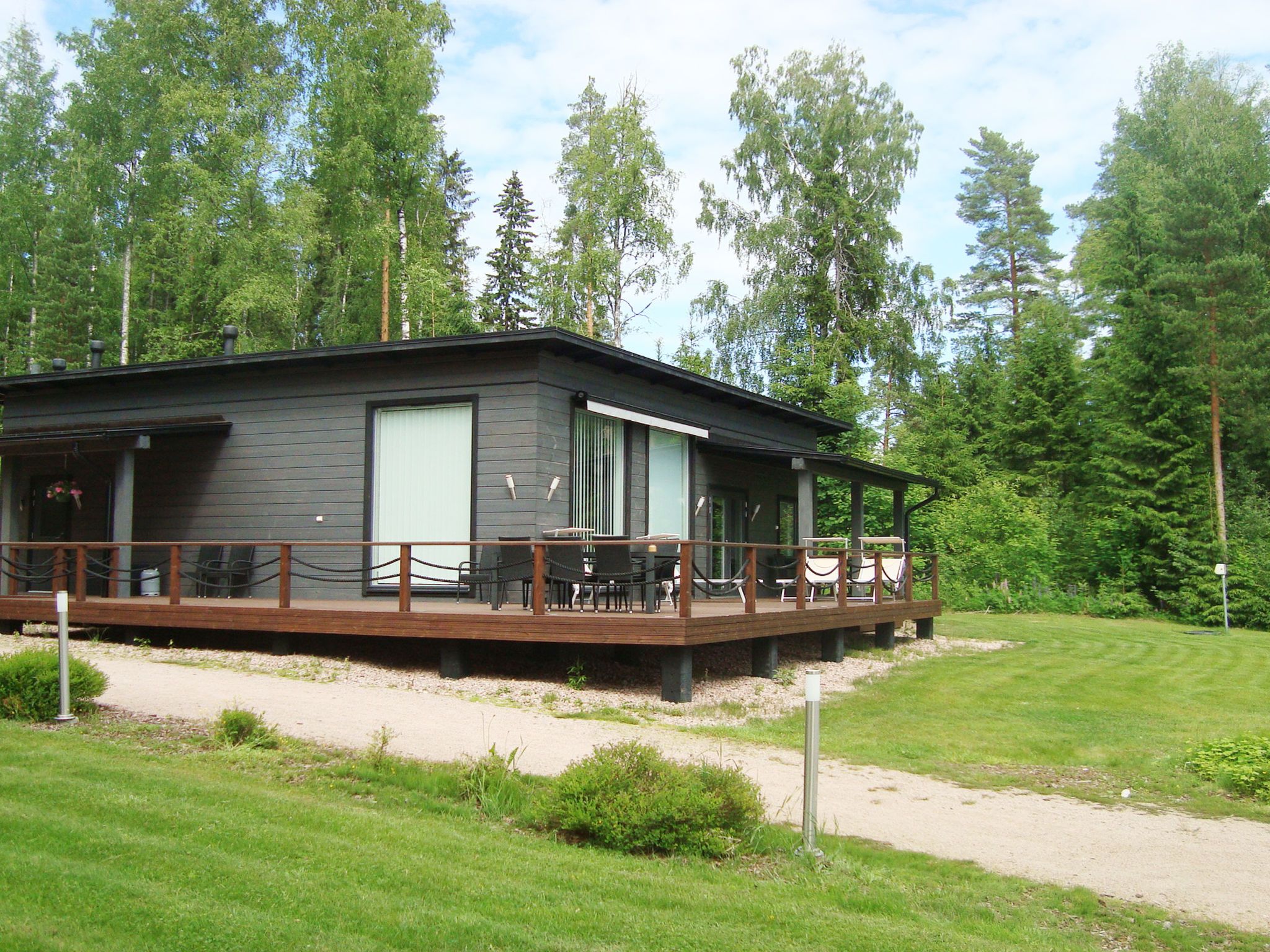 En modern stuga med en veranda, omgiven av en skog.