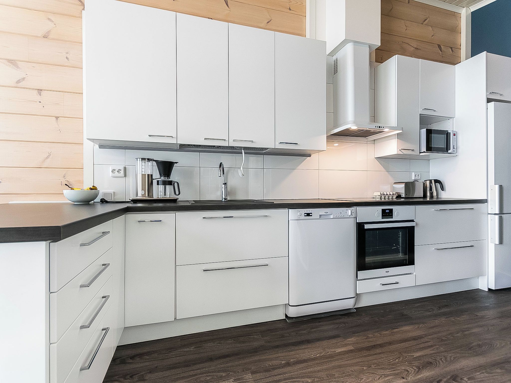 A modern kitchen with white cabinetry, a built-in oven, a microwave, and a coffee maker.