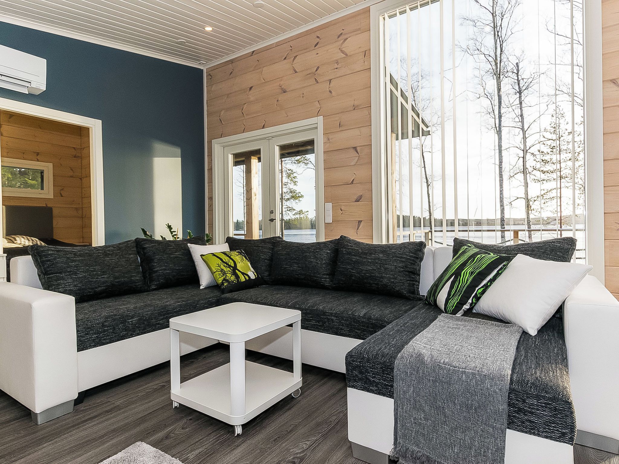 A modern living room with a sectional sofa, a white coffee table, and large windows offering a view of trees and a body of water.