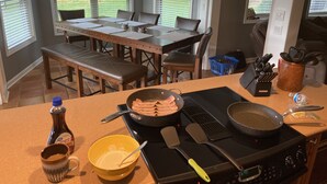 A kitchen with a dining table, chairs, a bench, a stove, cooking utensils, and a view of the backyard through large windows. - Discover Your Convenient Paradise: Minutes from I-65, Cullman, and Boat Launch (Cullman)
