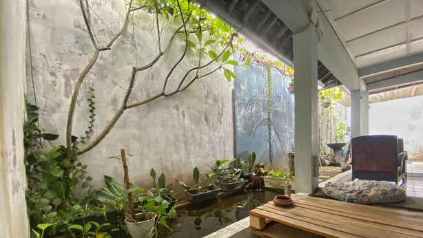 A small indoor garden with a water feature, wooden seating, and potted plants. - Reene'o Guesthouse (Yogyakarta)