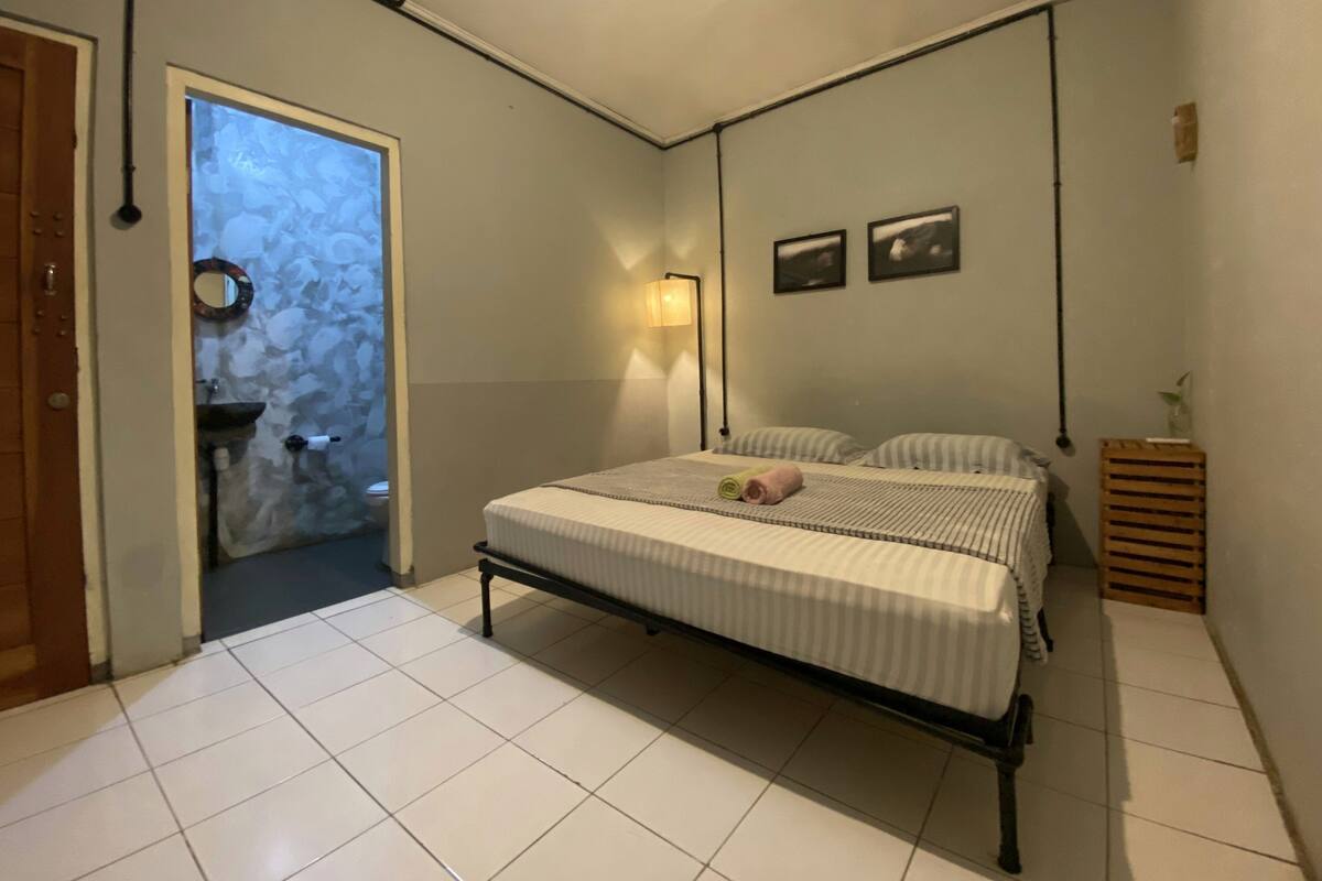 A bedroom with a bed, a bedside lamp, a small wooden side table, and a wall-mounted picture.