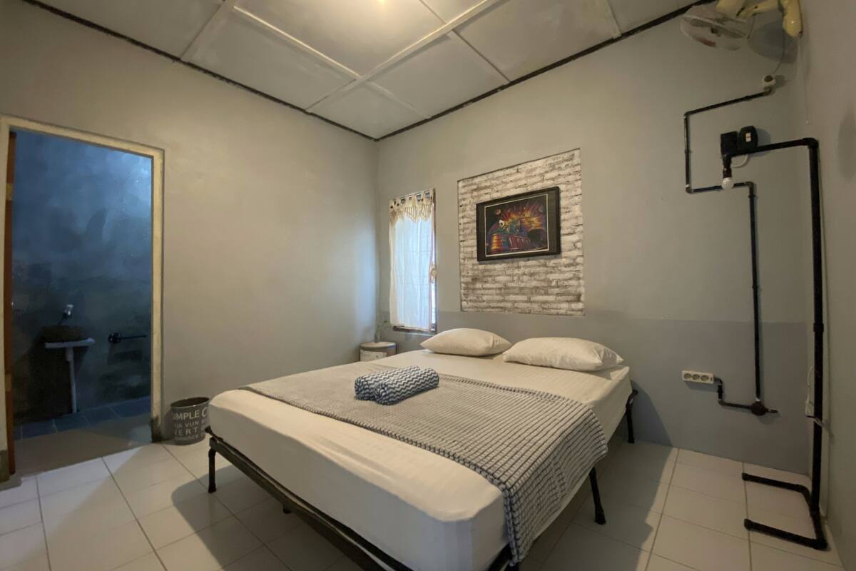 A bedroom with a bed, a nightstand, a wall-mounted picture, and a ceiling light.