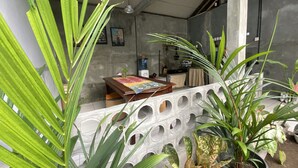 A room with a concrete wall, a wooden table with a colorful tablecloth, and potted plants. - Reene'o Guesthouse (Yogyakarta)