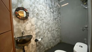 A bathroom with a stone wall, a sink, a toilet, and a mirror. - Reene'o Guesthouse (Yogyakarta)