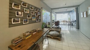 A spacious room with a long wooden table, books, a wall decorated with photos, and a view through a large window. - Reene'o Guesthouse (Yogyakarta)