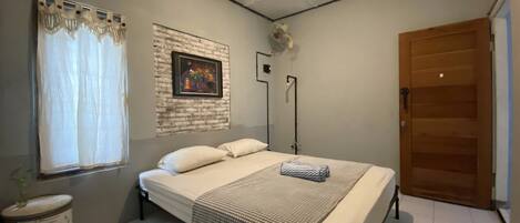 Un dormitorio con cama, ventana con cortinas, un cuadro en la pared, mesita de noche y una puerta.