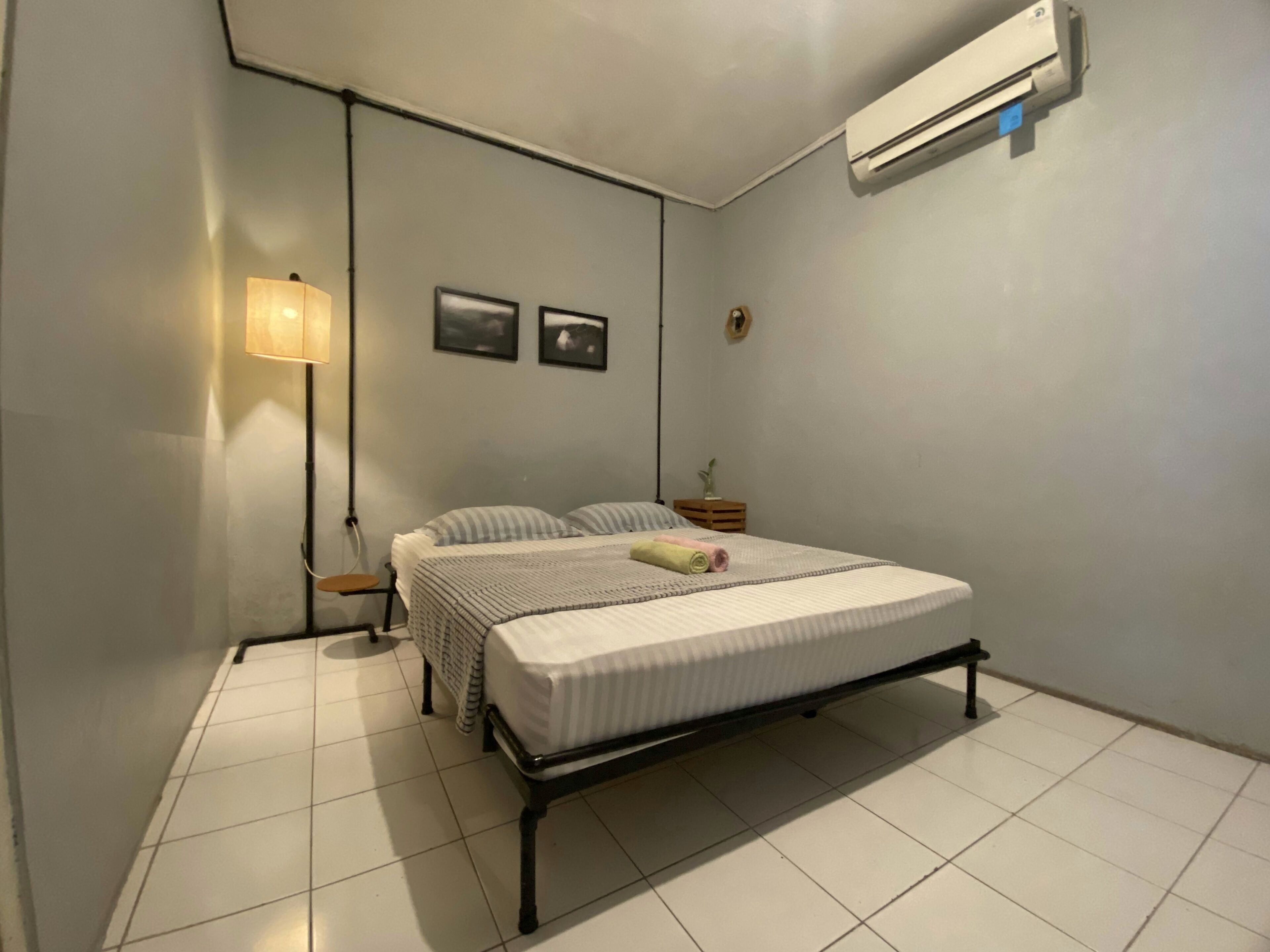 A bedroom with a bed, a nightstand, a lamp, and an air conditioning unit.