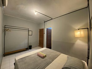 A bedroom with a bed, a bedside table, a hanging light fixture, and a door. - Reene'o Guesthouse (Yogyakarta)