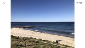 Ein Strand mit einem steinernen Wellenbrecher, sandigem Ufer und blauem Himmel.
