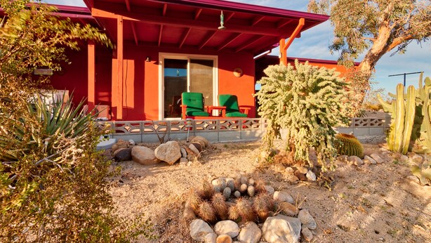 A red building with a covered patio, two green chairs, and a cactus in the foreground. - Chucks cabin Joshua Tree region, your desert Oasis (TWENTYNIN PLAMs)
