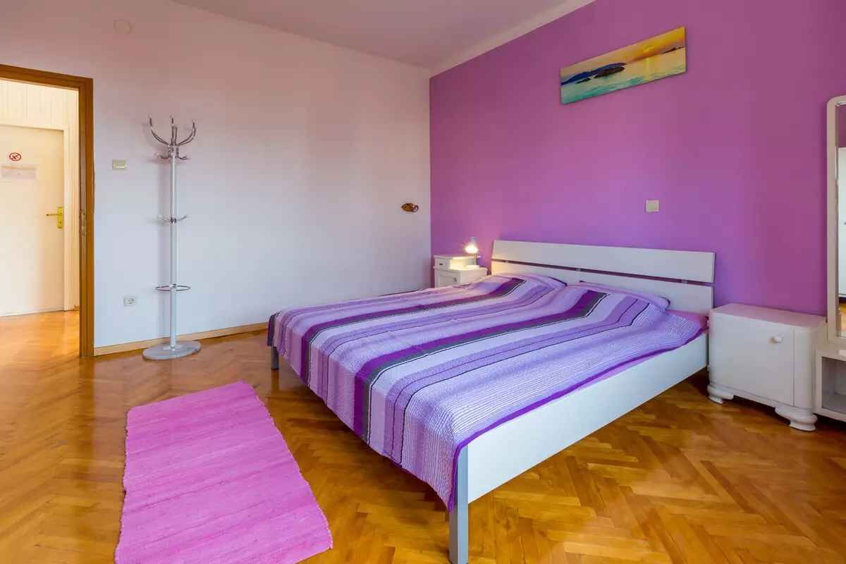Un dormitorio con cama, mesita de noche, lámpara, perchero y puerta.