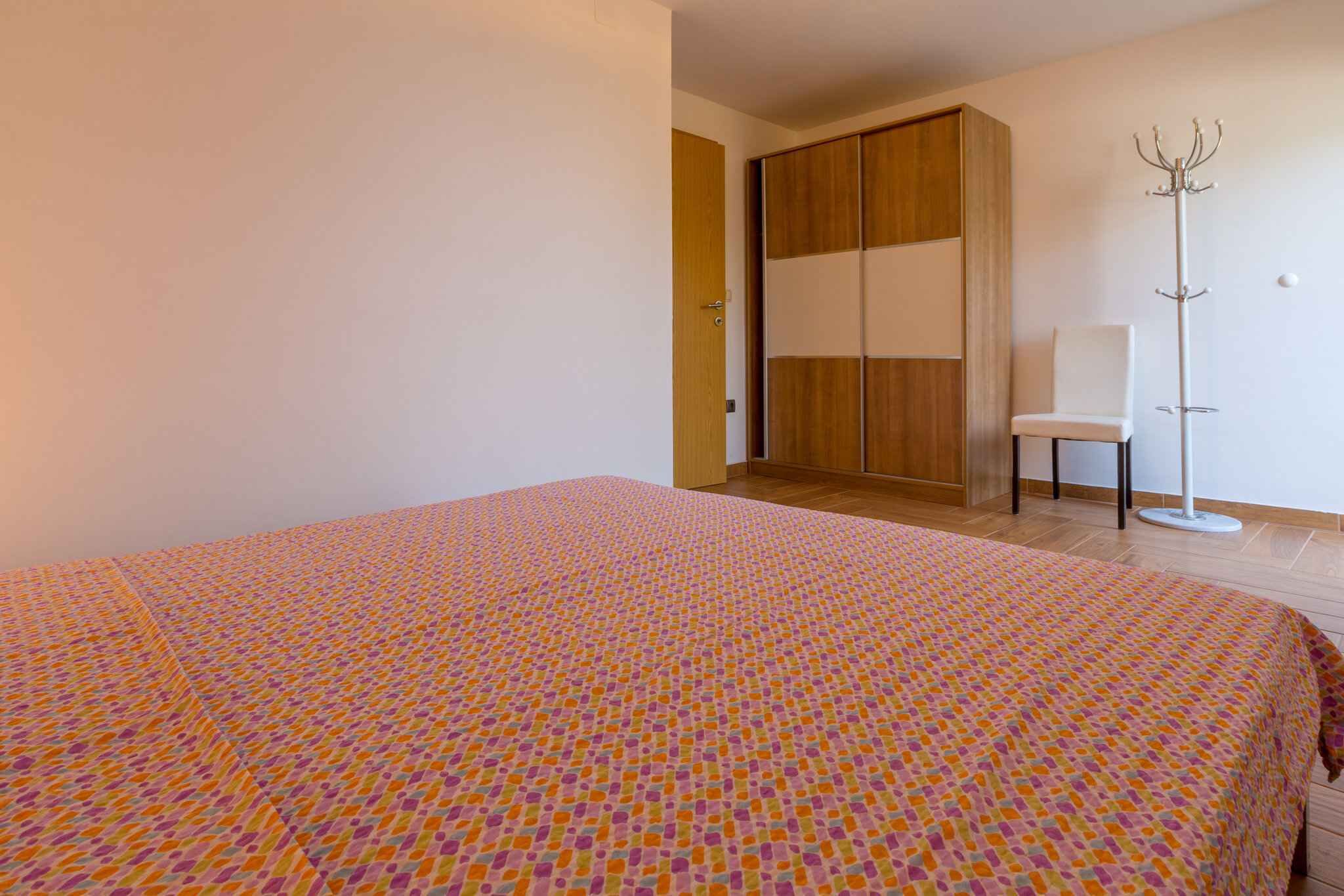 Une chambre à coucher comprenant un lit, une armoire, une chaise et un porte-manteau.