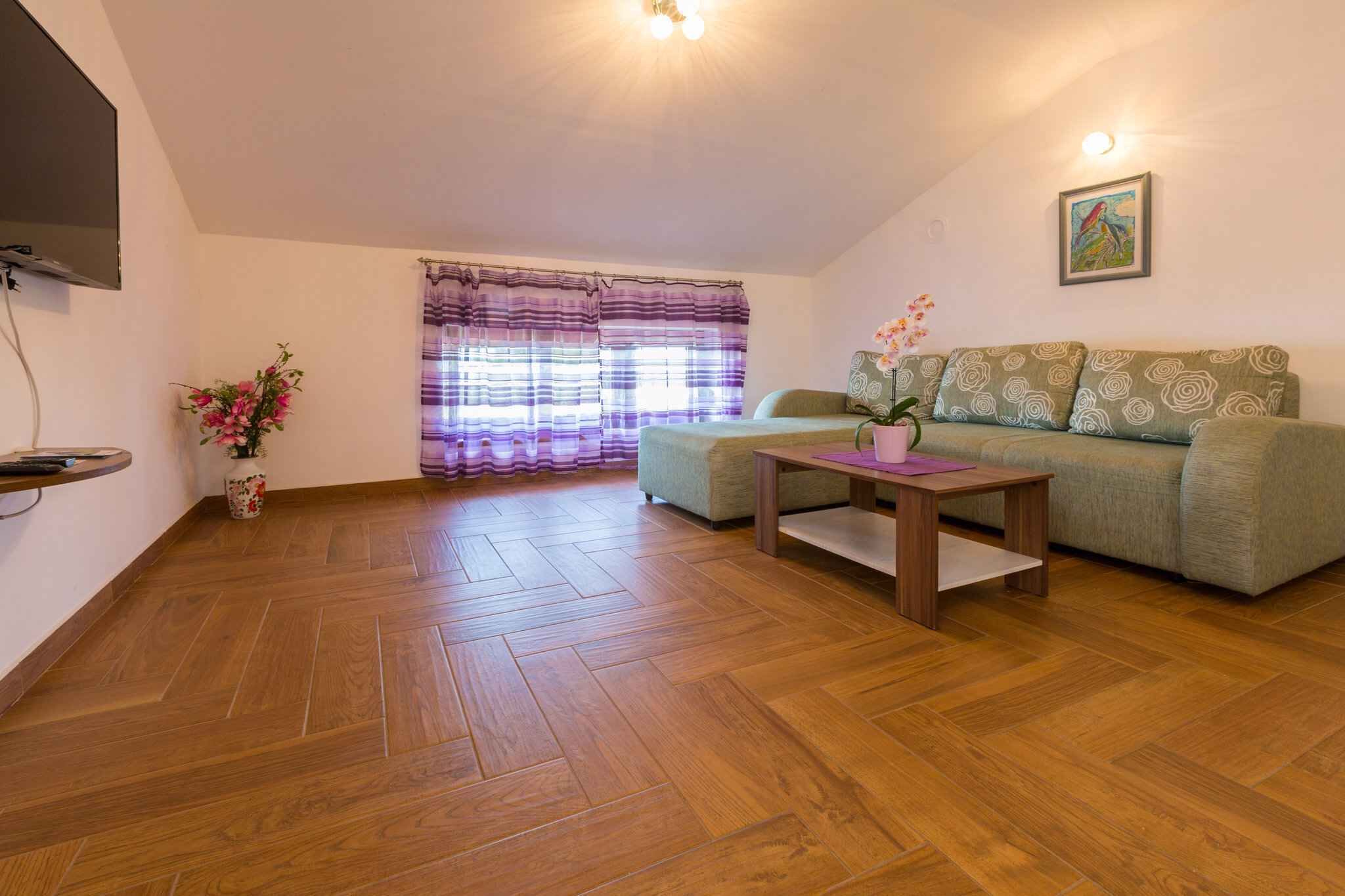 Un salon comprenant un canapé, une table basse, un téléviseur fixé au mur et une fenêtre avec des rideaux.