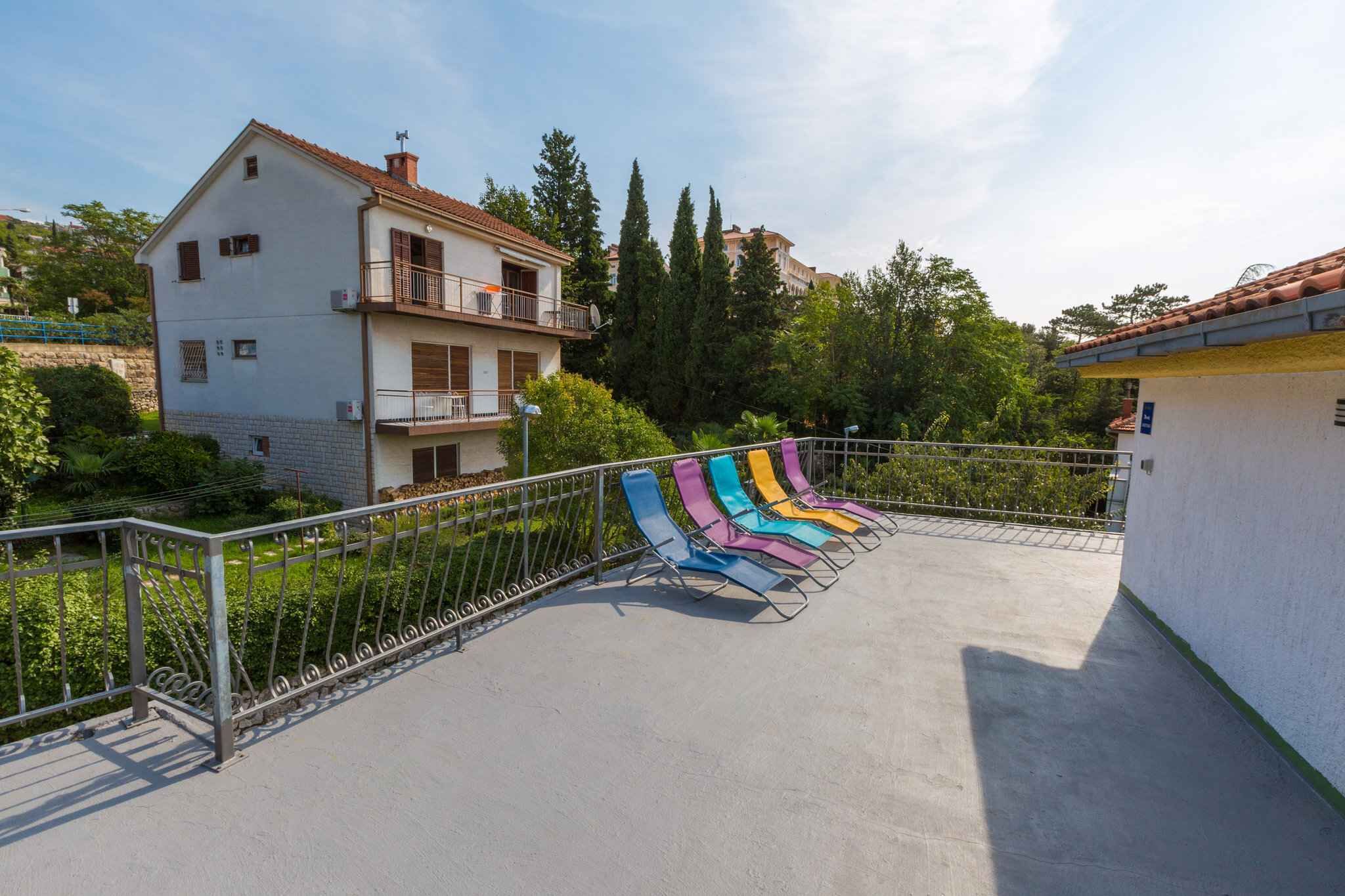 A residential building with a balcony, a concrete pathway, and a row of colorful lounge chairs.
