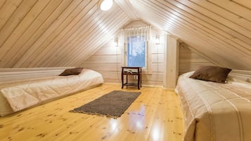 Ein kleines, gemütliches Schlafzimmer im Dachgeschoss mit Holzwänden und einer geneigten Decke. Zwei Betten mit Kissen und ein kleiner Tisch stehen in der Mitte.