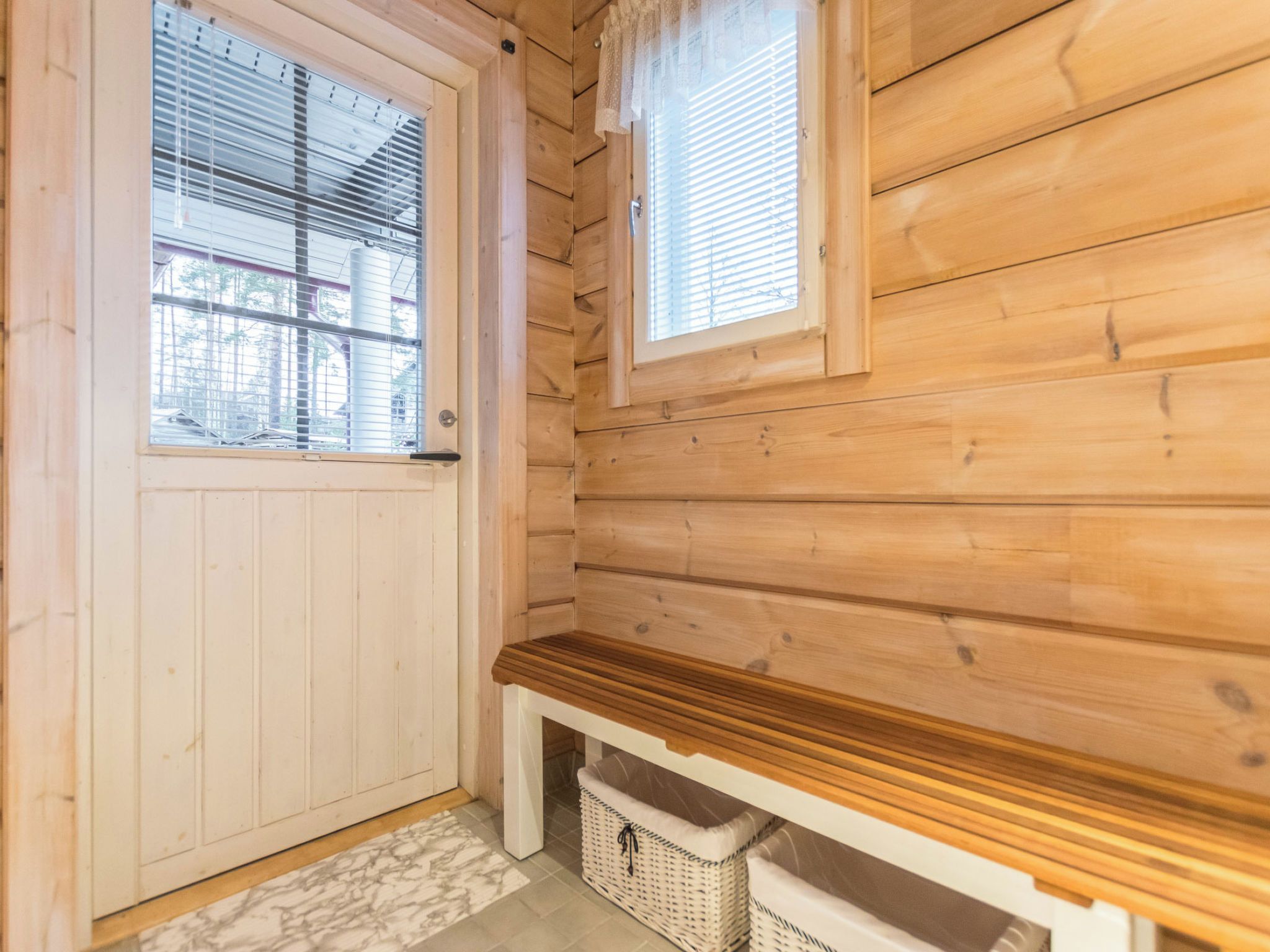 A wooden interior with a white door, a window with blinds, and a bench.