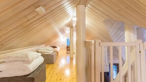 An attic bedroom with a sloped ceiling, wooden flooring, a bed with pillows, a small seating area, and a white gate.